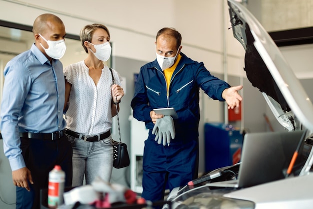 Reparador de automóviles explicando los problemas del motor a los propietarios de automóviles en un taller