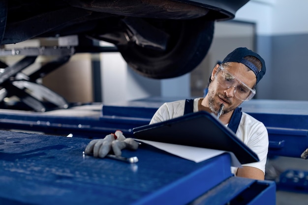 Reparador de automóviles tomando notas mientras examina un vehículo en un taller