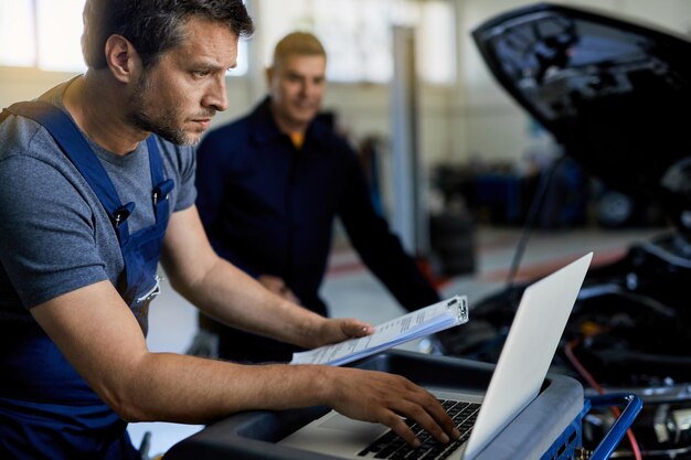 Reparador de automóviles trabajando en una computadora mientras realiza diagnósticos de automóviles con su compañero de trabajo en un taller