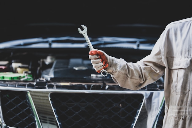 Reparador de automóviles con un uniforme blanco de pie y sosteniendo una llave que es una herramienta esencial para un mecánico