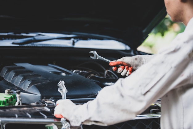 Reparador de automóviles con un uniforme blanco de pie y sosteniendo una llave que es una herramienta esencial para un mecánico