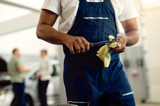 Reparador irreconocible que usa una llave mientras trabaja en el taller de servicio de automóviles