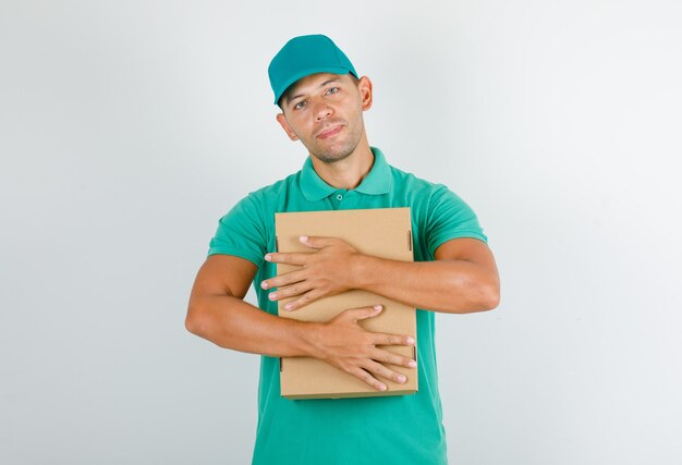 Repartidor abrazando caja de cartón en camiseta verde con gorra