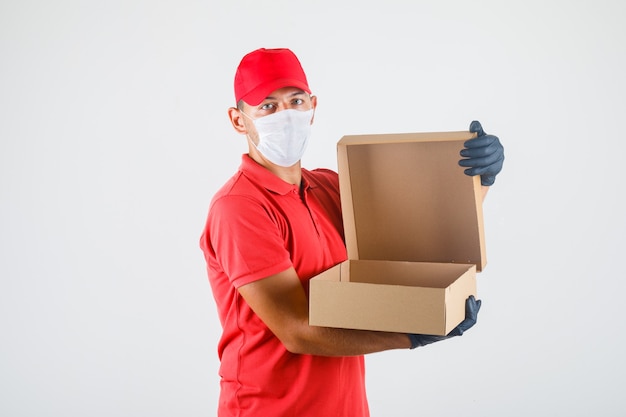 Repartidor abriendo caja de cartón en uniforme rojo, máscara médica, guantes
