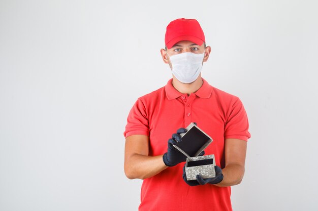 Repartidor abriendo caja presente en uniforme rojo, máscara médica, guantes.