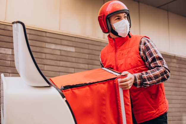 Repartidor de alimentos conduciendo scooter con caja con comida y máscara con máscara