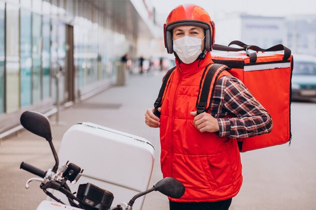 Repartidor de alimentos conduciendo scooter con caja con comida y máscara con máscara
