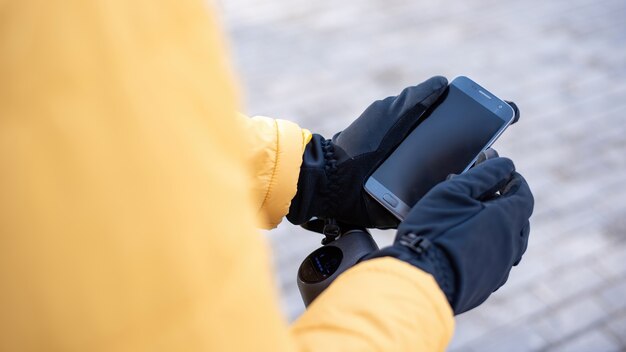 Repartidor de alimentos en un scooter con su teléfono inteligente. Chaqueta amarilla y guantes negros. Invierno