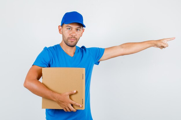 Repartidor apuntando hacia afuera y sosteniendo una caja de cartón en una camiseta azul