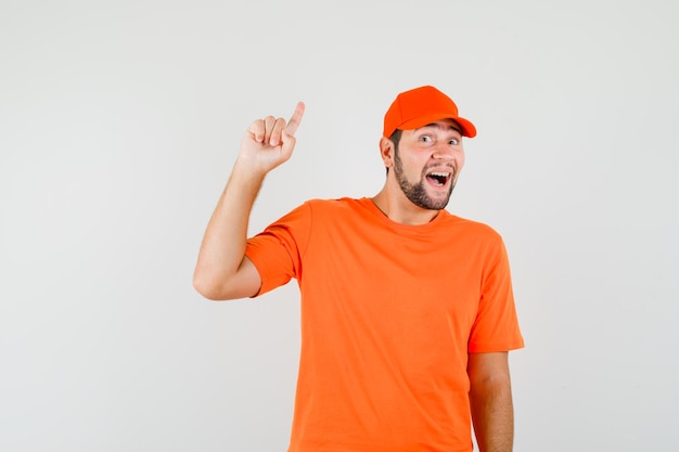 Repartidor apuntando con el dedo hacia arriba en camiseta naranja, gorra y mirando alegre, vista frontal.