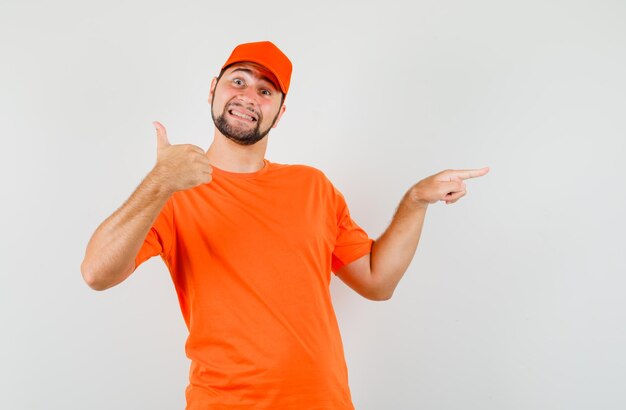 Repartidor apuntando hacia el lado con el pulgar hacia arriba en camiseta naranja, gorra y mirando alegre. vista frontal.