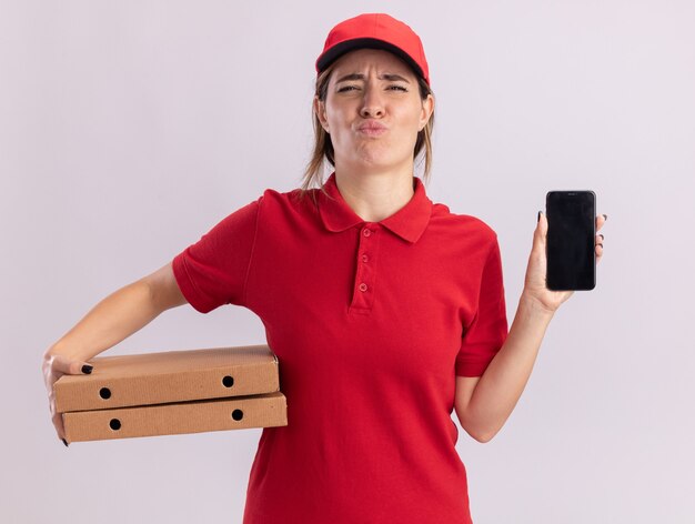 Repartidor bastante joven disgustado en uniforme tiene cajas de pizza y teléfono en blanco