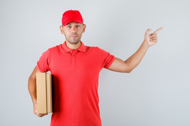 Repartidor con caja de cartón y apuntando hacia fuera en uniforme rojo