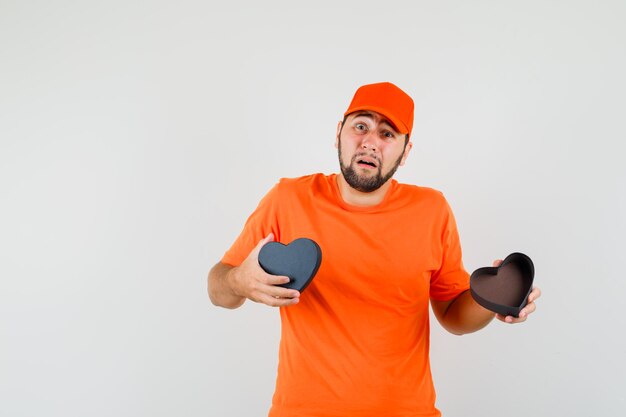 Repartidor con caja de regalo abierta en camiseta naranja, gorra y mirando abatido, vista frontal.