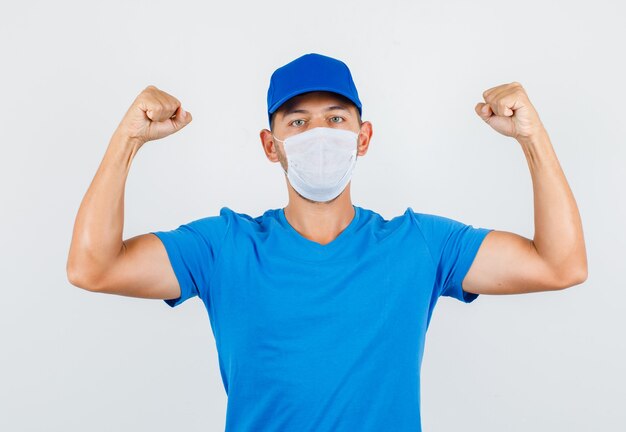 Repartidor en camiseta azul, gorra, máscara que muestra los músculos y parece fuerte