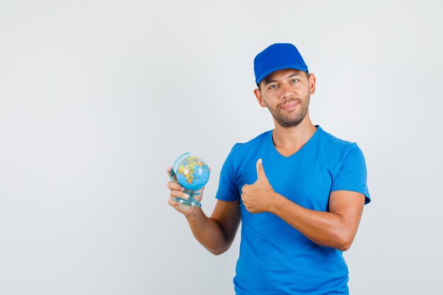 Repartidor en camiseta azul, gorra sosteniendo globo con pulgar hacia arriba y mirando alegre