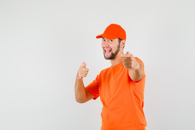 Repartidor en camiseta naranja, gorra apuntando y mirando feliz, vista frontal.