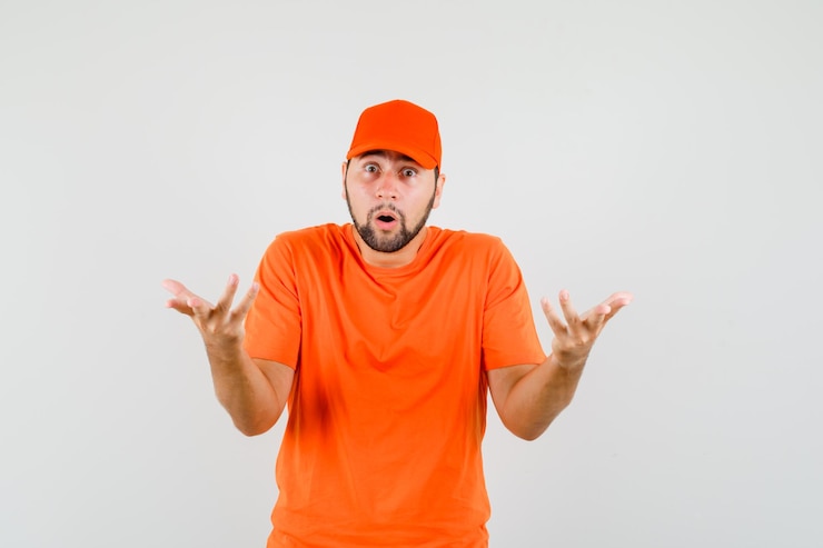 Foto gratuito repartidor en camiseta naranja, gorra manteniendo las manos en forma interrogativa y mirando perplejo, vista frontal.