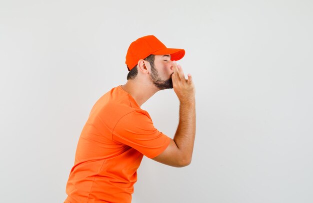 Repartidor en camiseta naranja, gorra mostrando gesto delicioso y mirando encantado.