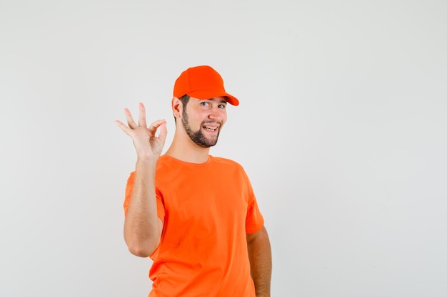 Repartidor en camiseta naranja, gorra mostrando gesto ok y mirando alegre, vista frontal.