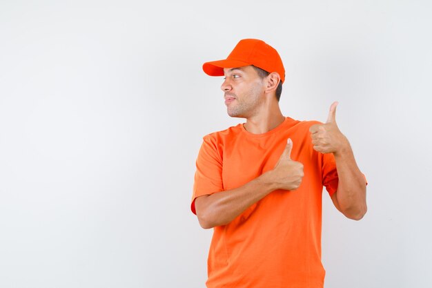 Repartidor en camiseta naranja y gorra mostrando los pulgares hacia arriba mientras mira a un lado y se ve alegre