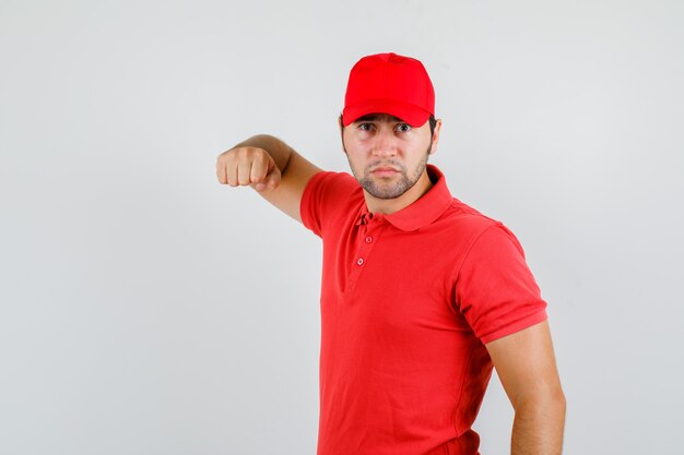 Repartidor en camiseta roja, gorra amenazando con puño y mirando furioso