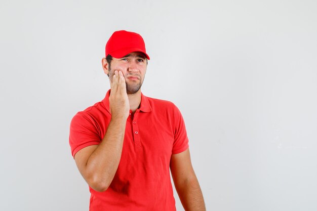 Repartidor en camiseta roja, gorra con dolor de muelas