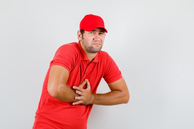 Repartidor en camiseta roja, gorra que sufre de dolor de estómago