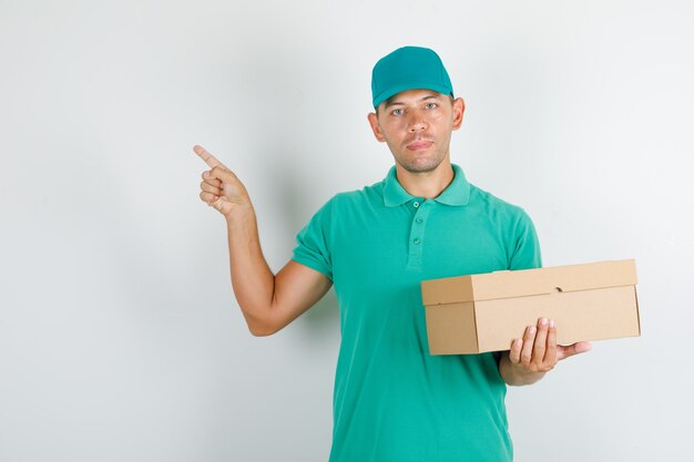 Repartidor en camiseta verde y gorra apuntando algo con caja de cartón