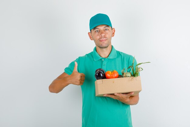 Repartidor en camiseta verde y gorra con caja de verduras con el pulgar hacia arriba