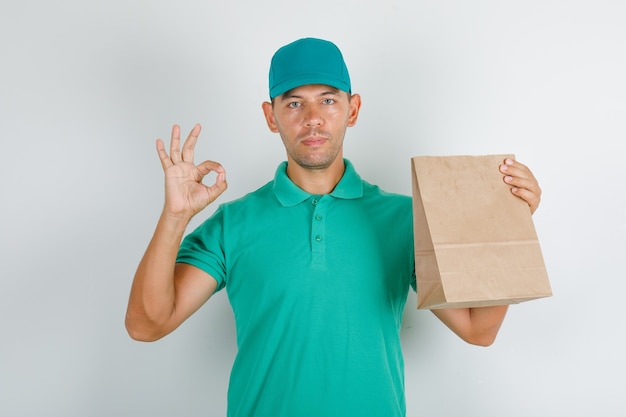 Repartidor en camiseta verde y gorra haciendo bien firmar con bolsa de papel