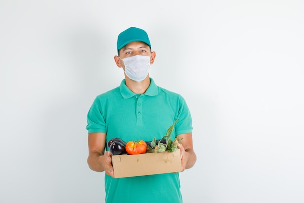 Repartidor en camiseta verde y gorra, máscara con caja de verduras