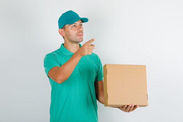 Repartidor en camiseta verde y gorra mostrando algo con caja de cartón