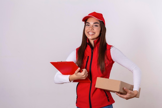 Foto gratuita repartidor entregando paquetes sosteniendo portapapeles y paquete sonriendo feliz en uniforme rojo hermosa mujer joven con máscara médica y guantes mensajero profesional aislado sobre fondo blanco