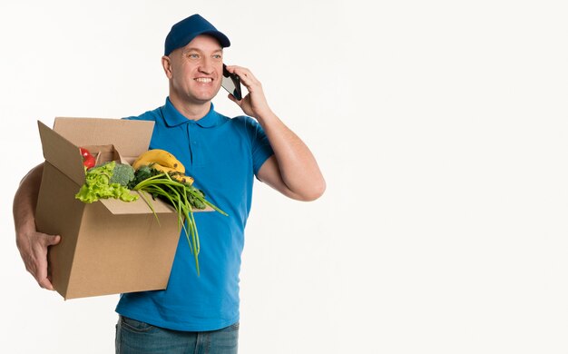 Repartidor feliz hablando por teléfono y sosteniendo la caja de supermercado