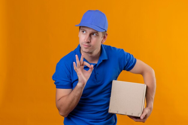 Repartidor guapo joven en uniforme azul y gorra con paquete de caja mirando a un lado