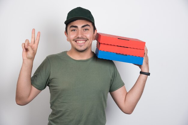 Repartidor haciendo cartel y sosteniendo tres cajas de pizza sobre fondo blanco.