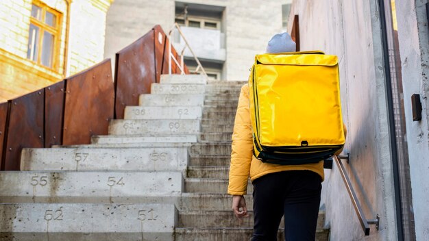 Repartidor en invierno con mochila amarilla subiendo las escaleras