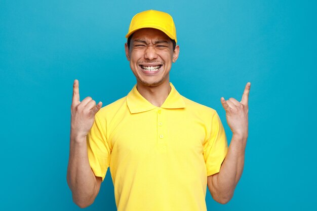 Repartidor joven agresivo con uniforme y gorra haciendo signo de rock