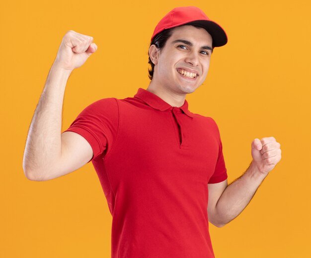 Repartidor joven alegre en uniforme azul y gorra mirando al frente haciendo gesto sí aislado en la pared naranja