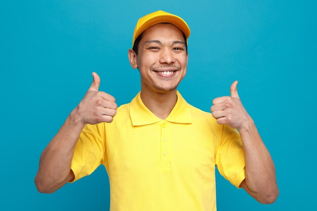 Repartidor joven alegre con uniforme y gorra mostrando los pulgares para arriba