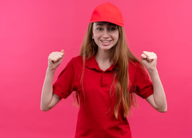 Repartidor joven alegre en uniforme rojo con los puños levantados en el espacio rosa aislado