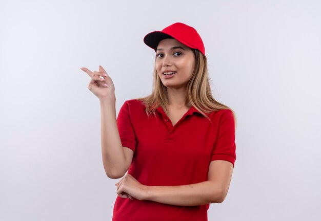 Repartidor joven complacido con uniforme rojo y puntos de gorra al lado aislado en la pared blanca con espacio de copia