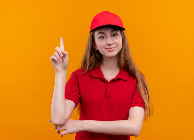 Repartidor joven confiado en uniforme rojo con el dedo levantado en el espacio naranja aislado