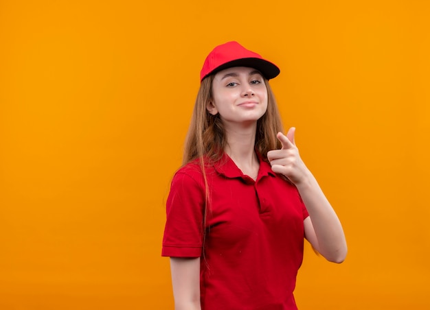 Repartidor joven confidente en uniforme rojo que le hace gesto en el espacio naranja aislado con espacio de copia