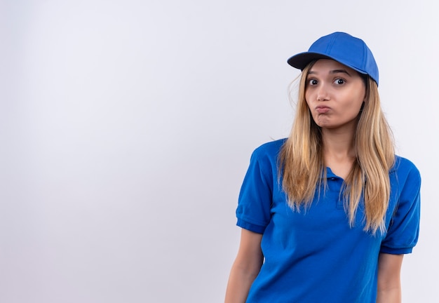 Repartidor joven descontento con uniforme azul y gorra aislado en la pared blanca con espacio de copia