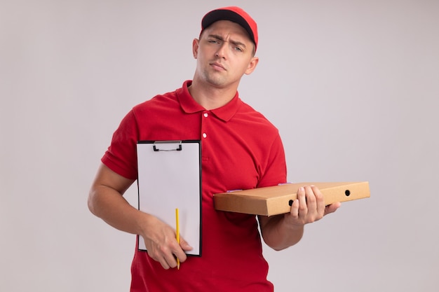 Repartidor joven disgustado con uniforme con gorra sosteniendo el portapapeles con caja de pizza aislado en la pared blanca