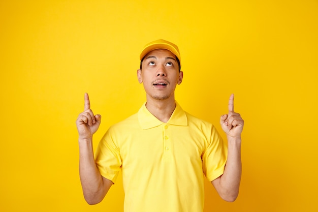 Repartidor joven impresionado con gorra y uniforme apuntando hacia arriba