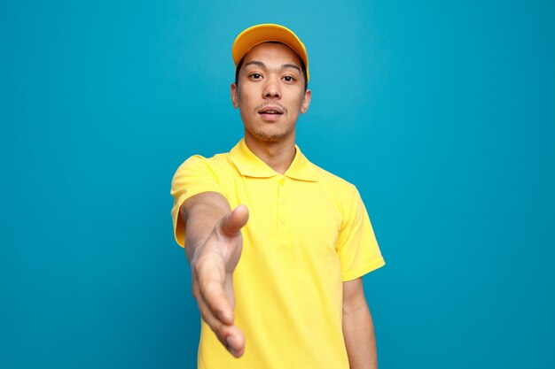 Repartidor joven impresionado con uniforme y gorra haciendo gesto de saludo