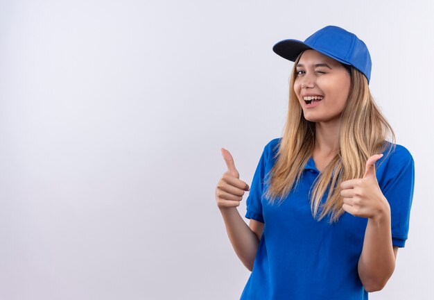 Repartidor joven parpadeando, vistiendo uniforme azul y gorra con el pulgar hacia arriba